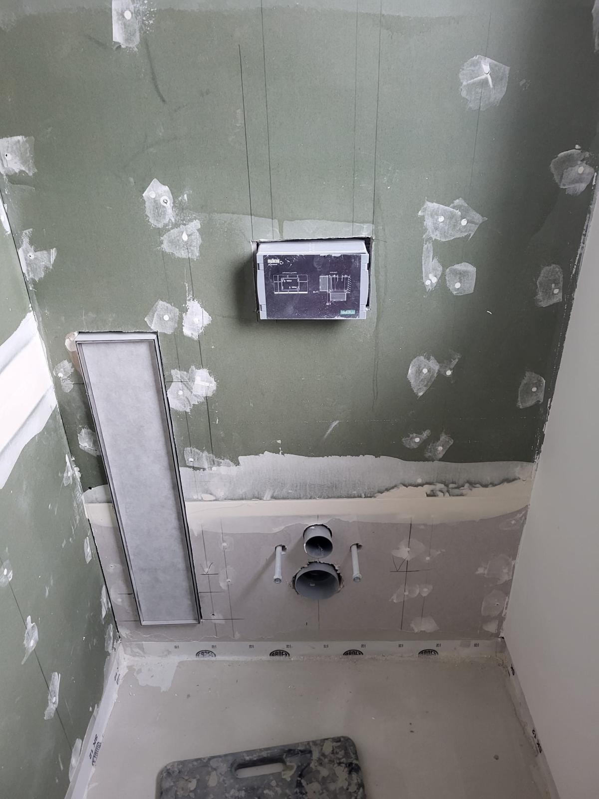 Toilettenelement mit Aufbewahrungsfach Unfertig verputzte Wand in einem Badezimmer mit Abfluss und Steuerungselement.