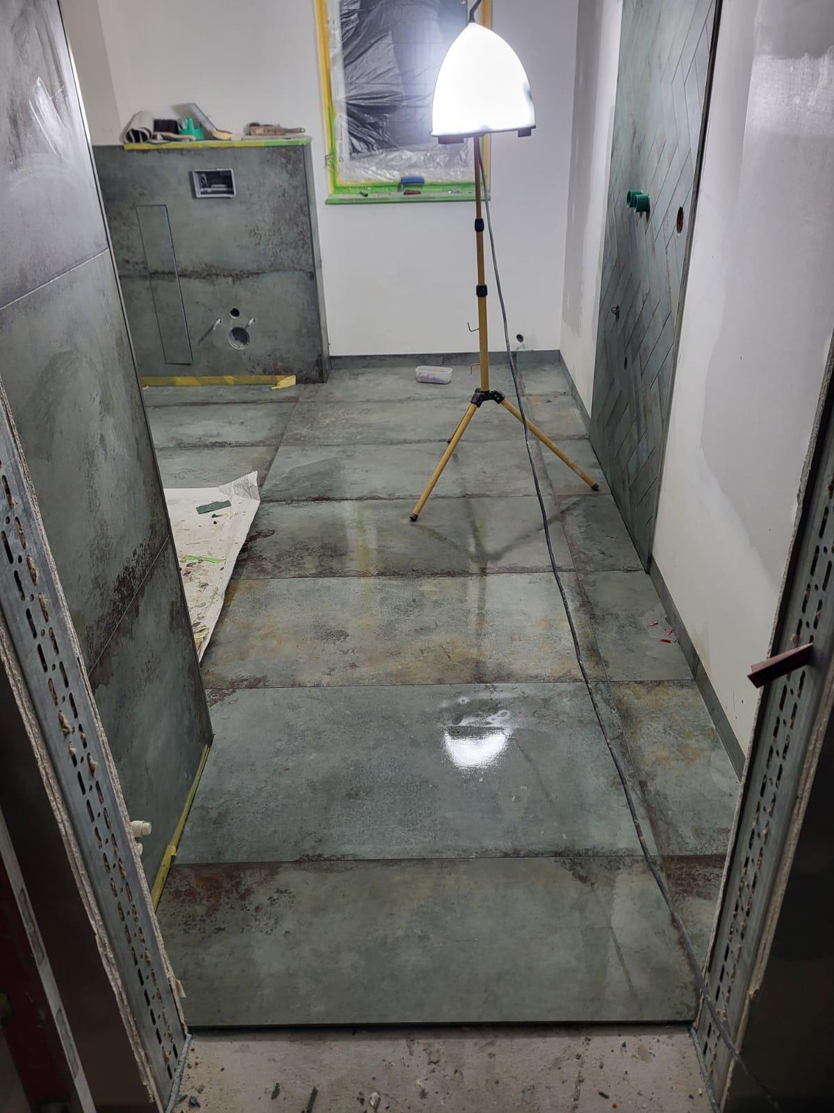 Frisch verfugtes Bad Boden eines Raumes mit frisch gegossenem Beton und einem Beleuchtungsständer.