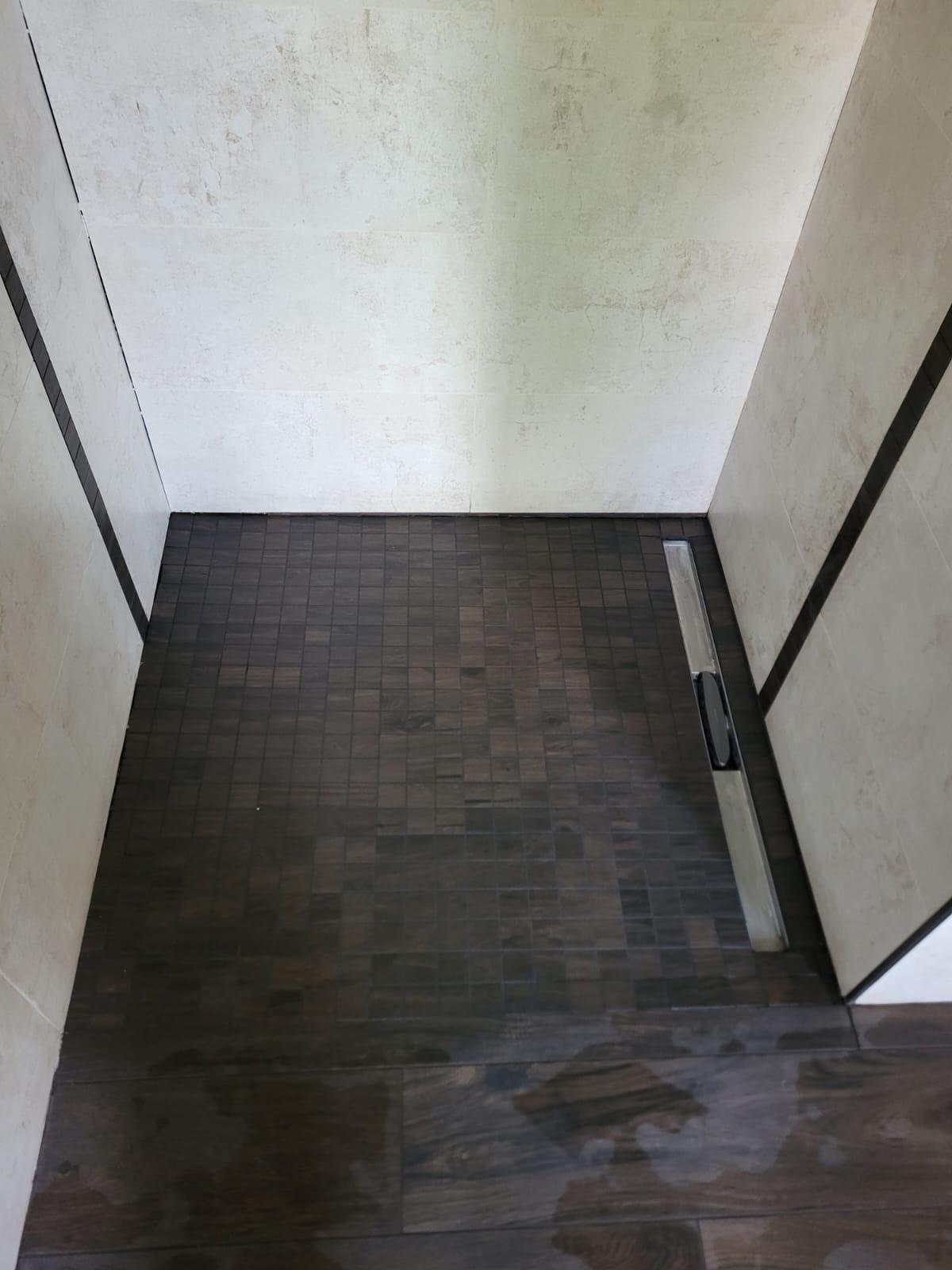 Dusche mit Mosaikbelag Holzboden in einer modernen Dusche mit grauer Wandverkleidung.